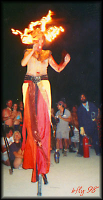 The Wise Woman with headdress of fire while stiltwalking